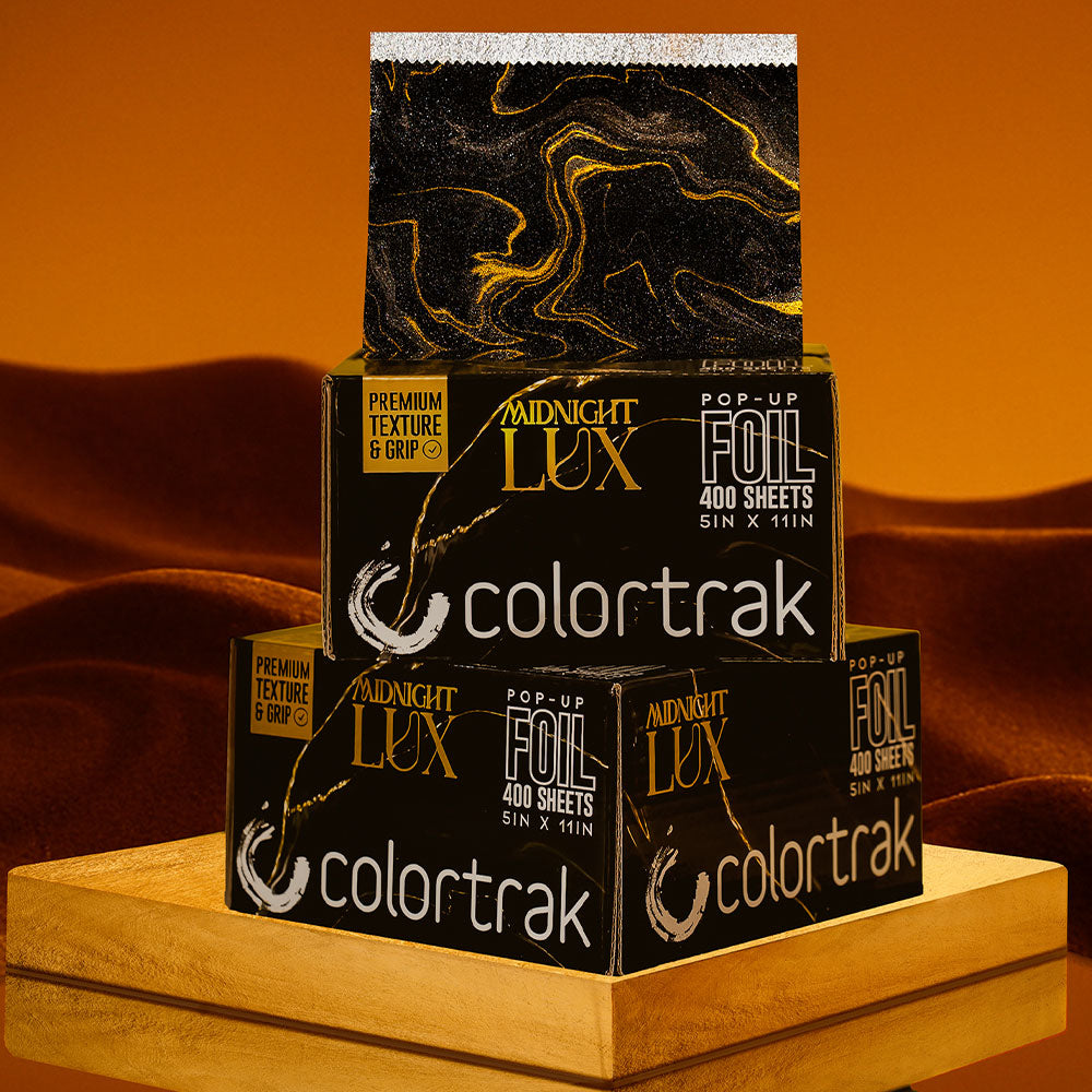 Stack of Colortrak paper boxes with gold foil design on a wooden surface.