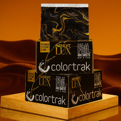 Stack of Colortrak paper boxes with gold foil design on a wooden surface.